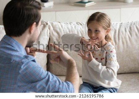 Happy pretty daughter kid and father talking with gestures, speaking sign language at home. Therapist training smiling child with hearing disability, deafness to use hands, fingers for communication Royalty-Free Stock Photo #2126195786