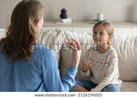 Female therapist teaching pretty kid girl to speak gestures language. Teacher and child practicing speaking, sign communication, vocal exercises, correct pronouncing, foreign language skills Royalty-Free Stock Photo #2126196005