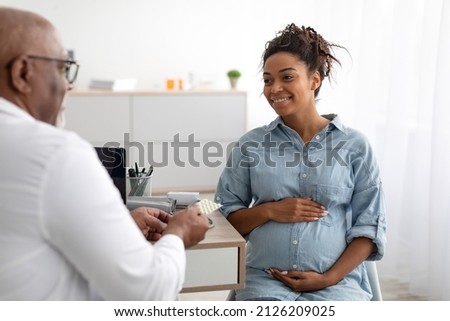 Pregnancy, Obstetrics, Gynaecology, Medicine, Healthcare And People Concept. Black male gynecologist giving pills to smiling pregnant woman during appointment at hospital. Visit To A Doctor Concept Royalty-Free Stock Photo #2126209025