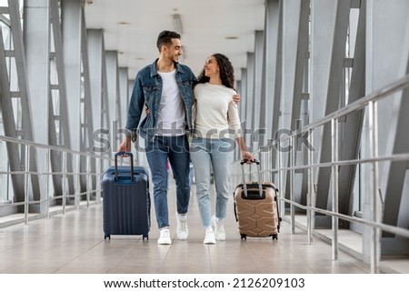 Trip Together. Happy Young Arab Spouses Walking With Luggage At Airport Terminal, Romantic Middle Eastern Couple Embracing And Smiling To Each Other While Going To Boarding Gate, Copy Space Royalty-Free Stock Photo #2126209103