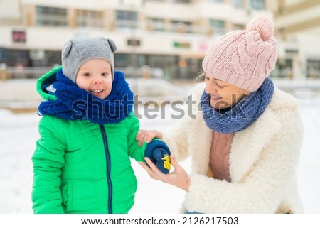 mom puts mittens on her son and laughs around the city in winter.