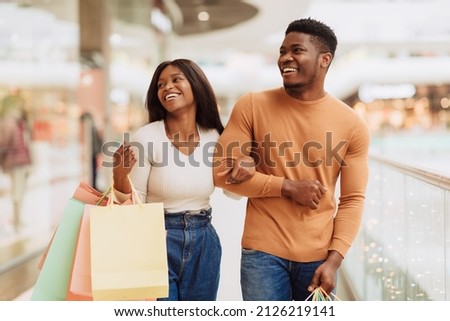 Portrait of beautiful millennial African American guy and lady shopping on weekend, walking in the city mall with colorful bags, looking at boutique window and laughing spending time together Royalty-Free Stock Photo #2126219141
