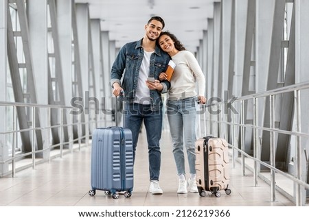 Portrait Of Cheerful Young Middle Eastern Couple Standing At Airport With Luggage And Smartphone, Millennial Arab Man And Woman Air Travelling Together, Ready For Vacation Trip, Copy Space