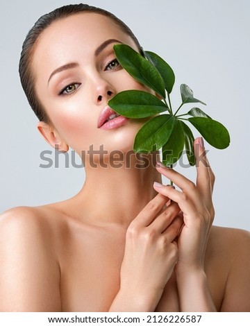 Young beautiful woman with green leave near face and body. Skin care beauty treatments concept.  Closeup girl's face with green leave. White model with clean, health skin of face - posing at studio Royalty-Free Stock Photo #2126226587