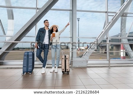 Vacation Offer. Portrait Of Joyful Young Arab Couple Waiting For Flight At Airport, Happy Middle Eastern Spouses With Suitcases Standing In Terminal And Pointing Aside, Ready For Travel, Copy Space Royalty-Free Stock Photo #2126228684