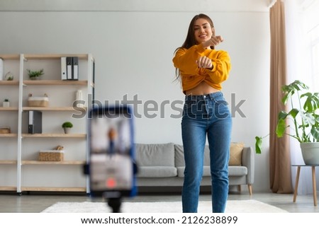 Millennial female lifestyle blogger filming video on cellphone, dancing on webcam at home. Cheerful young influencer live streaming for her entertainment blog, shooting for social network