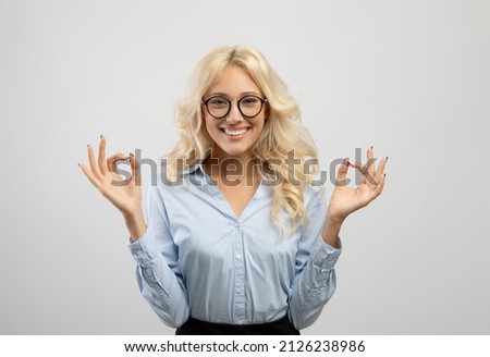 Coping with stress at work. Young caucasian businesswoman meditating after busy day, doing breathing exercises and smiling at camera over light grey background
