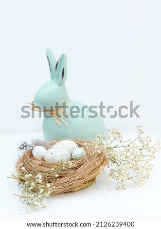Decorative hare, Easter bunny and Easter eggs in straw on a light background with copy space. Vertical Easter photo.