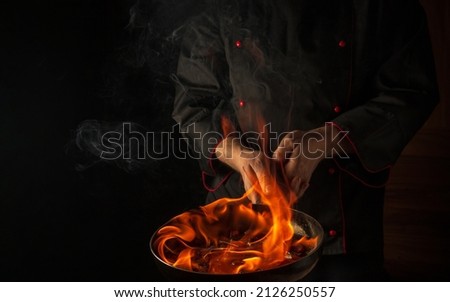 The chef cooking food in pan with fire flame on black background. Restaurant and hotel service concept. European cuisine.