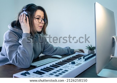 A young woman creates music using a musical keyboard and a computer.