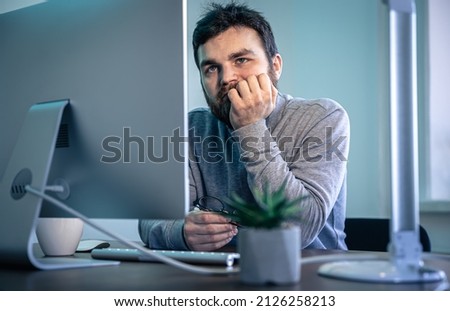 Tired bearded man looks at the computer screen.