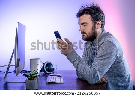 A man sits in front of a computer, uses a smartphone, workplace.
