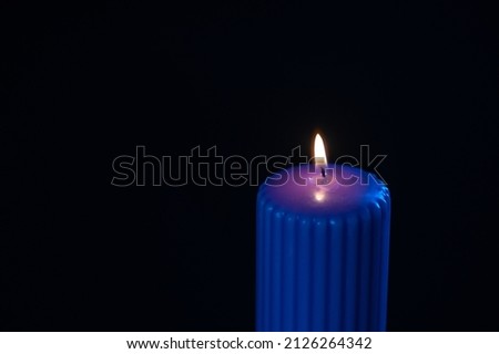 Blue purple candle with orange flame over black background