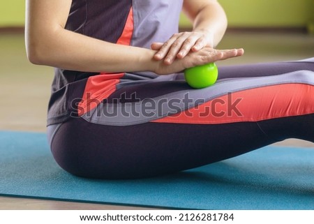 Woman in sportswear, performs myofascial relaxation of the thigh muscles with a massage ball, sits on a mat in the room, close-up