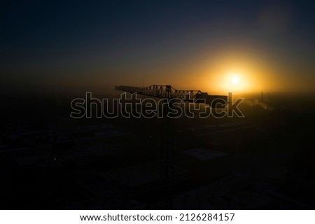 Industrial construction cranes and building silhouettes over sun at sunrise. Royalty-Free Stock Photo #2126284157
