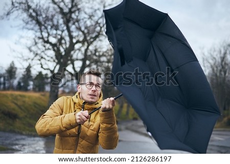 Man holding broken umbrella in strong wind during gloomy rainy day. Themes weather and meteorology. 