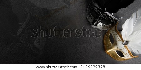 Venetian black, gold and white masks on dark silver glitter background. New year, Christmas, Purim, Mardi Gras party celebration design banner. Carnival masquerade costume ball Royalty-Free Stock Photo #2126299328