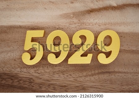 Wooden numerals 5929 painted in gold on a dark brown and white patterned plank background.