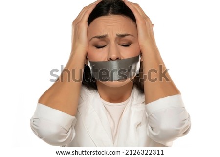 Unhappy young woman with adhesive tape over her mouth on a white background Royalty-Free Stock Photo #2126322311