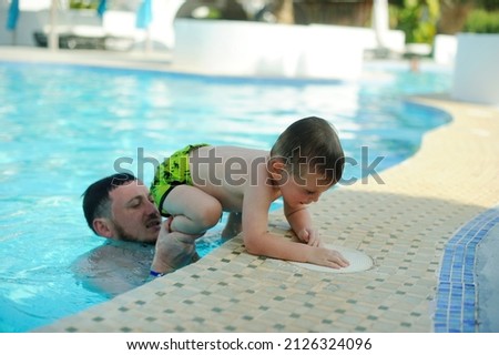 Dad and toddler son play and swim in the resort pool