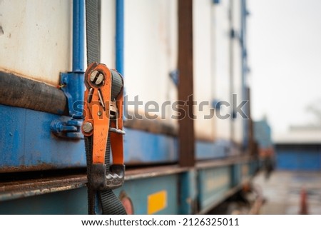 Webbing belt strap lashing to secure container or load which is prepared for transport on the truck. Safety in transportation industrial scene photo. Close-up and selective focus at the object part. Royalty-Free Stock Photo #2126325011