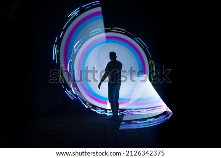 one person standing against beautiful blue green and red circle light painting as the backdrop

