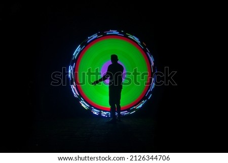 one person standing against beautiful purple green and red circle light painting as the backdrop

