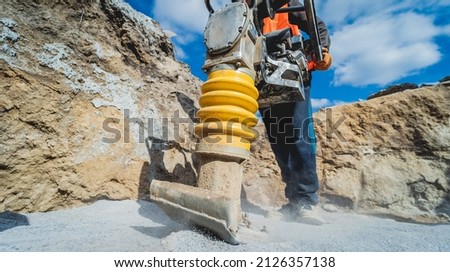 Worker uses a portable vibration rammer at construction of a power transmission substation Royalty-Free Stock Photo #2126357138