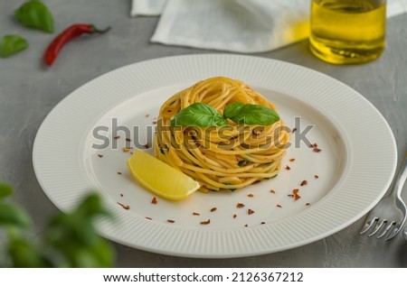 Spaghetti aglio e olio spaghetti aglio olio e peperoncino white plate lemon basil chili flakes parsley grey background Royalty-Free Stock Photo #2126367212