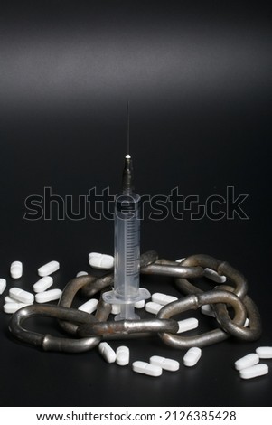 White tablets. Medical syringe and metal chain. Symbol of drug addiction. On a black background.