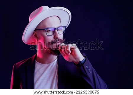 Portrait of sceptic Hipster bearded man with mustache in white wide-brimmed hat and blazer in glasses who looking away holds fist on chin. color filters. Men's style. 