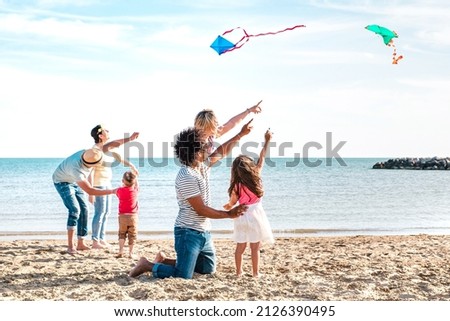 Multiple mixed families composed by parents and children playing with kite at beach vacation - Summer joy life style concept with candid people having fun together at seaside - Bright vivid filter Royalty-Free Stock Photo #2126390495