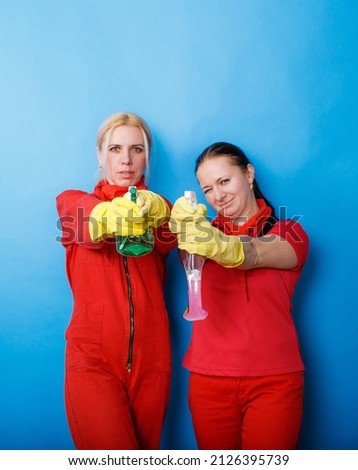 Two girls cleaning company workers in red uniforms smile on an isolated blue background. Cleaning and cleaning concept Royalty-Free Stock Photo #2126395739