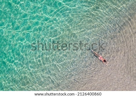 Top, aerial view. Young beautiful woman in a red bikini panties lying and sunbathe in sea water on the sand beach. Drone, copter photo. Summer vacation. View from above. 