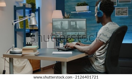 Man working as videographer editing video montage of people dancing on computer while using headphones. Media editor doing retouch work and visual effects on footage for film production