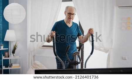 Retired man doing cardio exercise with stationary bicycle to have workout training activity. Pensioner using electric machine to cycle and do gymnastics. Old person with fitness bike. Royalty-Free Stock Photo #2126401736
