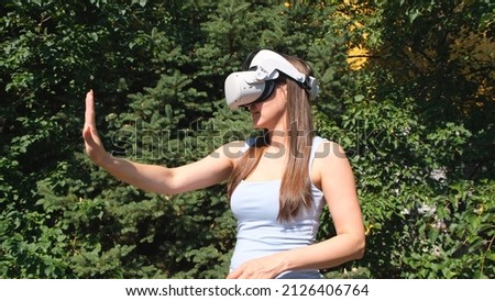 Female in virtual reality glasses controls the device with his hands against the background of green trees.