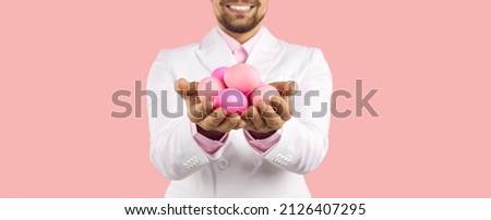 Cropped shot of a happy man smiling and holding a pile of beautiful traditional pink fresh Easter eggs in his hands. Easter traditions concept. Banner background