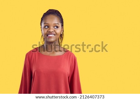 Portrait of cute and funny unsure african american woman biting her lip on yellow background. Close up of young beautiful woman in red blouse looking away at copy space. Banner. Isolated. Royalty-Free Stock Photo #2126407373