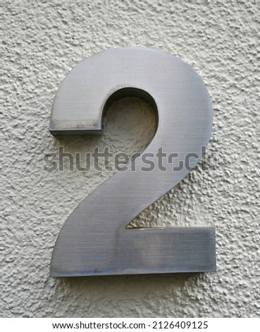 A silber metallic number two (number 2) on a greay wall  