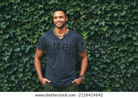 Outdoor portrait of young handsome african americam man, wearing black t-shirt, posing next to green ivy wall