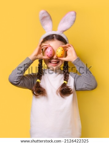 Funny happy girl with Easter bunny ears and colorful Easter eggs on a yellow background. Happy Easter! Copy space.