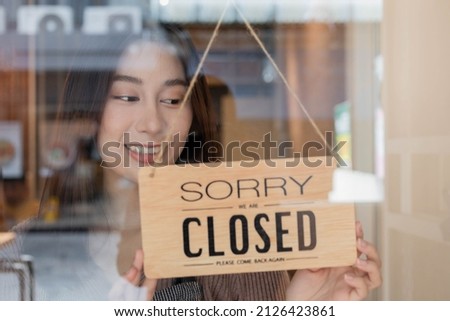 Pretty asian young owner retail, coffee shop woman turning sign board to closed after finished work, job and protection to pandemic of coronavirus. Close store due to lockdown, quarantine of covid.