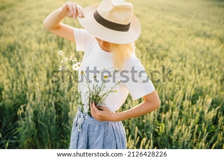 Gorgeous and creative caucasian woman decorate dress from chamomile cinching with belt around waste outfit, standing in wheat field at summer time in sunset. Woman unity nature concept.