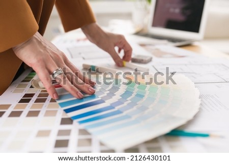 Close-up of architect woman choosing samples of wall paint. Interior designer looking at color swatch for creating project. House renovation, architecture and interior design concept.