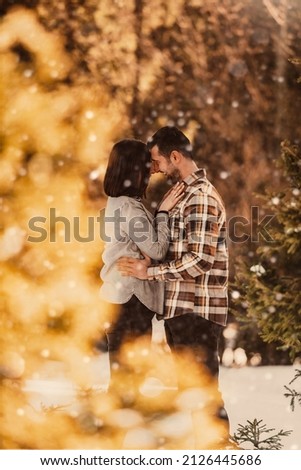 Beautiful couple hugging between snowy pines, a woman in casual clothes holding hands-on man chest. Selective focus. High-quality photo