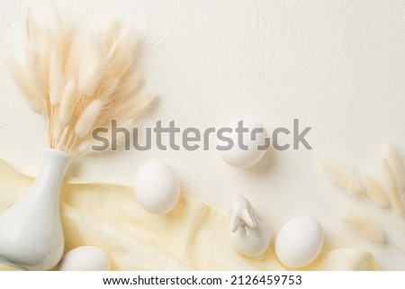 Top view photo of easter decorations white vase with lagurus flowers ceramic bunny easter eggs and cloth on isolated white background with copyspace
