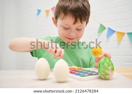 cute smiling boy 4-5 years old paints an easter egg with yellow paint. The child is busy with creativity, decorating eggs for the holiday. Horizontal photo. Royalty-Free Stock Photo #2126478284