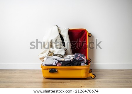 Open yellow suitcase with clothes on a wooden floor against a white wall