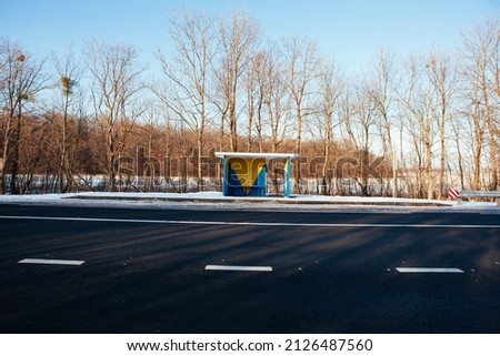 modern bus shelter with glass design and billboard poster holder case in the winter in residential urban setting with bare trees, salty sidewalk, wood garbage bin and snowy background. polar vortex.